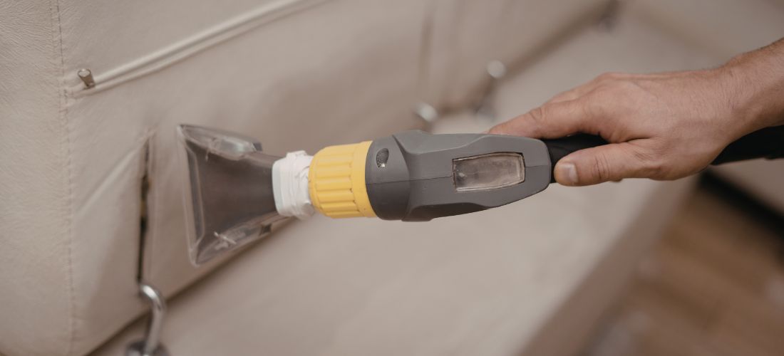 Tita Kleans employee deep cleaning the back of a sofa using a steam cleaner from Karcher.